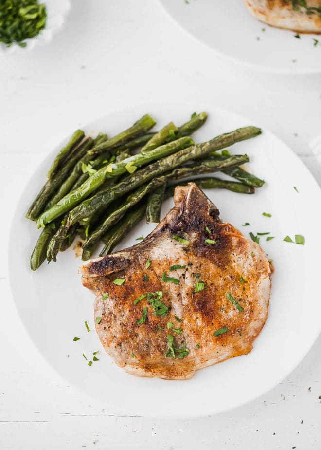 baked bone-in pork chops on a plate with green beans side