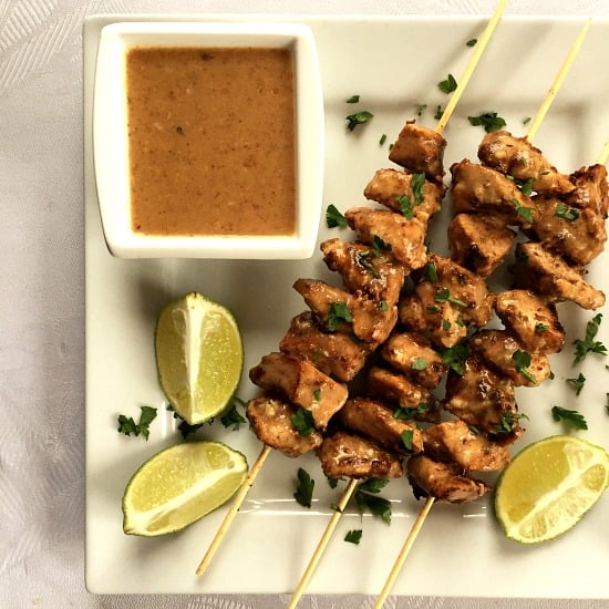 Overhead shoot of a white plate with chicken stay skewers, a bowl of peanut sauce and 3 lime wedges