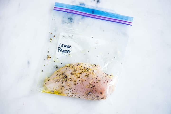 Sealable freezer bag with chicken breast and lemon pepper chicken marinade, marinating and ready to cook.