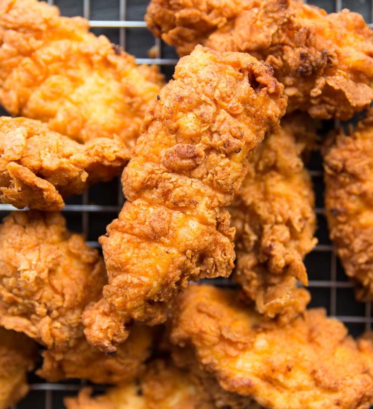 overhead shot of chicken tenders resting on a wire rack, focus on one tender surrounded by the rest.