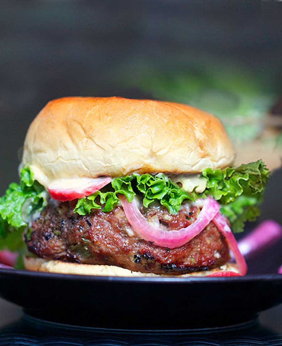 Korean BBQ Burger on a bun with pink pickled onions and radishes and lettuce