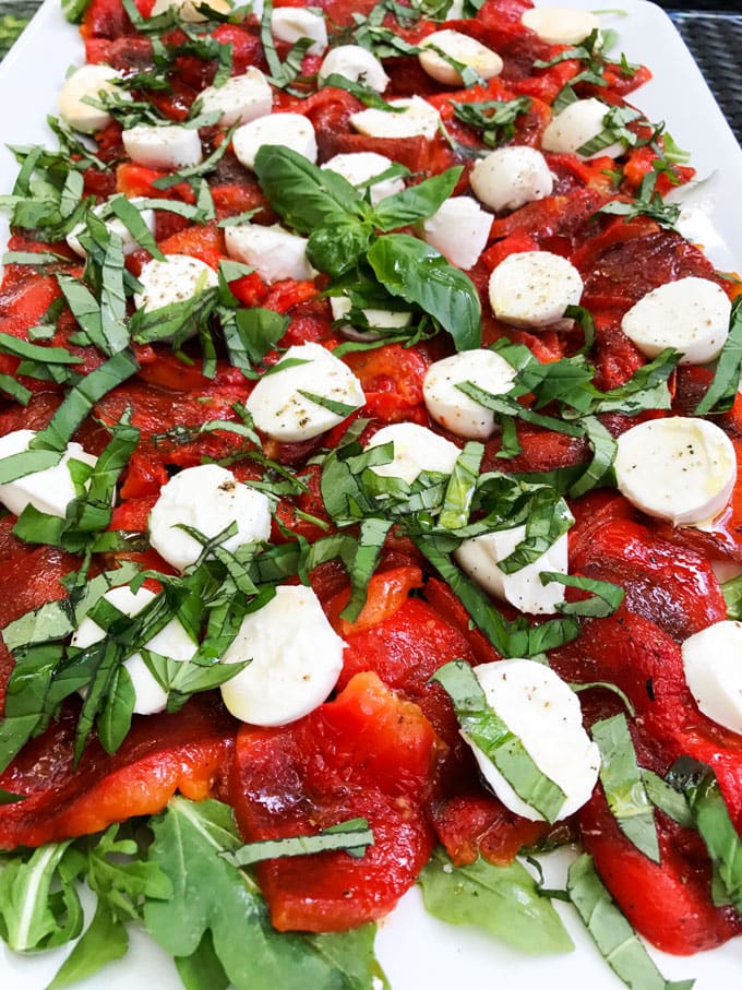 a platter of roasted red peppers with arugula and mozzarella cheese